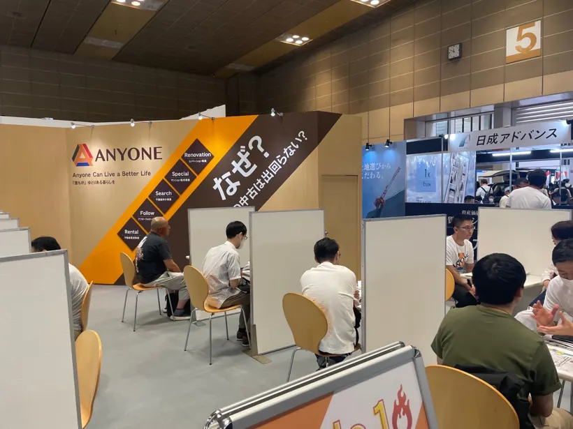 資産運用EXPOのANYONEブースで、営業社員が来場者に個別にご案内している風景