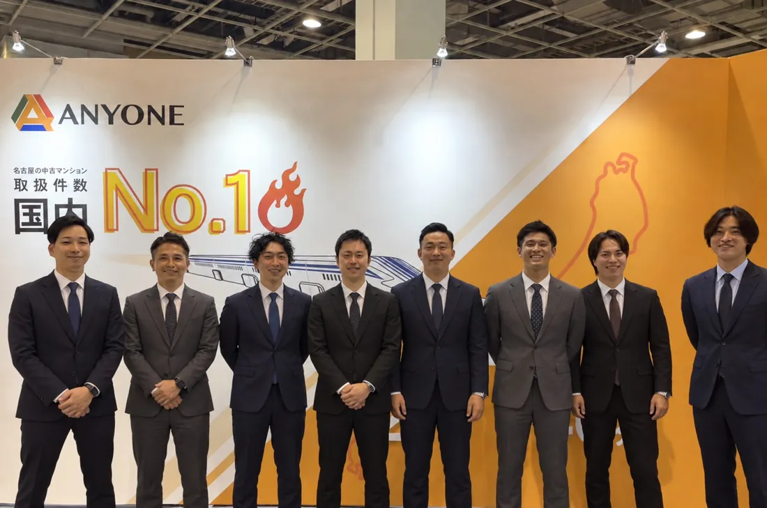 資産運用EXPOのANYONEブースに並ぶ営業チーム8名の集合写真